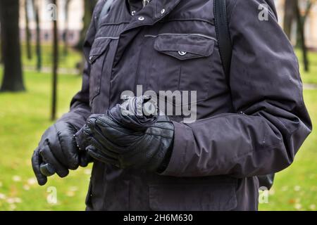 Close-up of man's hand in jacket and gloves holding closed umbrella Stock Photo