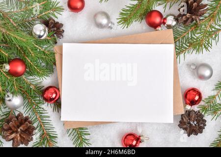 One empty card is lying on a kraft envelope in the snow with a Christmas tree and glass balls. Banner, invitation, postcard. Flatlay, Flatlay, Flatlay Stock Photo