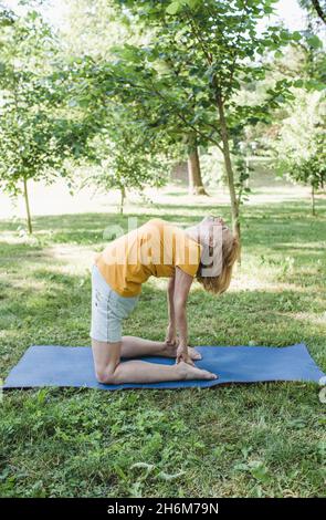 Portrait of an elderly woman sitting on a yoga mat and doing sports in the park. Stock Photo