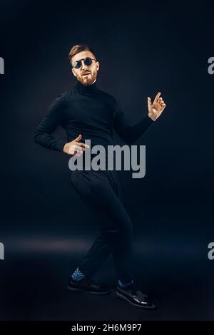 Happy funny hipster guy in black performing show dance who isolated on black studio background. Stock Photo