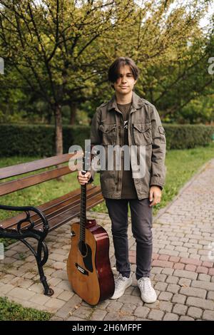 Portrait of long hair boy hold acoustic guitar. Young boy preparing for playing guitar outdoor Stock Photo