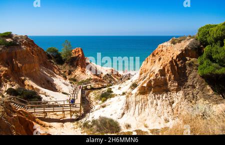 Orange cliffs ending in the blue sea with tourists on a footbridge at 'Falesia' in Algarve, Portugal