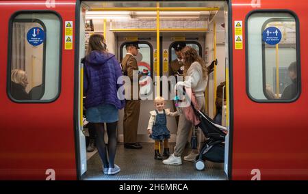 A young girl looks out of a London tube train as it waits on a District & Circle Line platform on 14 Nov 2021. Two soldiers in uniform stand behind. Stock Photo