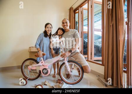 smiling father, mother and daughter holding new mini bike assembled Stock Photo