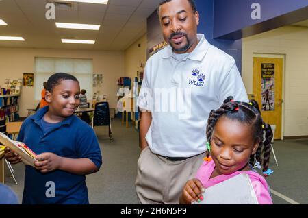 A male teacher helps elementary school students choose library books in the school library, Oct. 4, 2011, in Columbus, Mississippi. Stock Photo