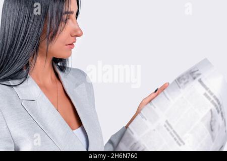 Side view photo of a pretty business woman with black long hair in a light jacket holding a newspaper and reading the article. Stock Photo