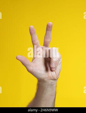Male hand gesture close-up on yellow background. Man hand isolated showing three fingers. Stock Photo
