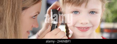 Woman pediatrician looking at eardrum of little girl using otoscope in clinic Stock Photo