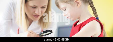 Doctor pediatrician examining rash on skin of hand of little girl using magnifying glass Stock Photo