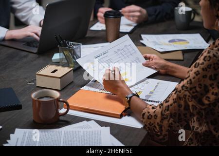 Close-up of businesswoman examining financial report and discussing it with her colleagues during a meeting at office Stock Photo