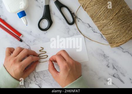 DIY ribbon rope, scissors used to create individual greeting card merry christmas. Christmas tree made of rope. Top view of hands making step by step Stock Photo