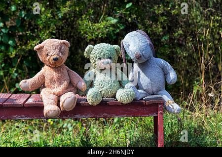 Three different coloured stuffed animals, teddy bears sitting together on a red bench, Gotland, Sweden Stock Photo