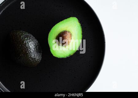 Ripe avocado halves on black plate, top view Stock Photo