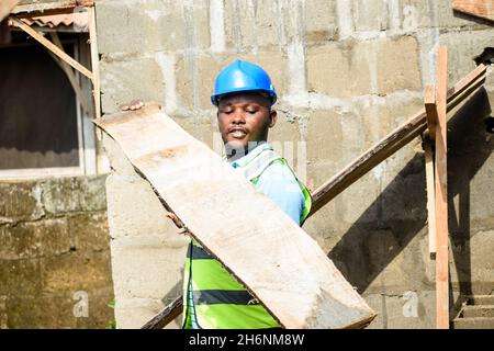 African male construction worker with a helmet working with a plank on a building site in Nigeria Stock Photo