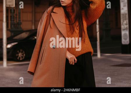 Cropped figure of a young woman in a brown cozy autumn warm coat and knitted sweater. Street casual fashion. Film grain effect Stock Photo