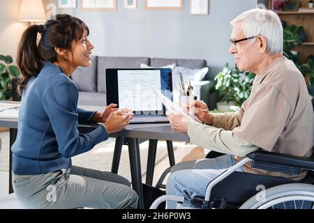 Senior man in eyeglasses discussing business contract together with his assistant while they sitting in the room at home Stock Photo