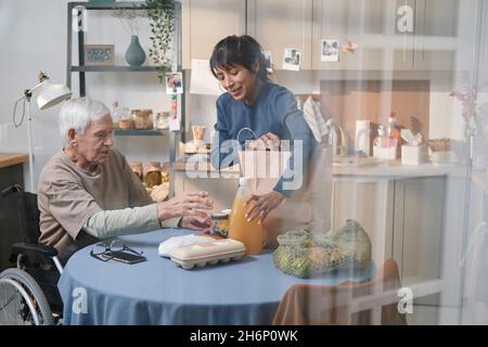 Volunteer taking the food out of the paper bag, she helping the senior man to buy products Stock Photo