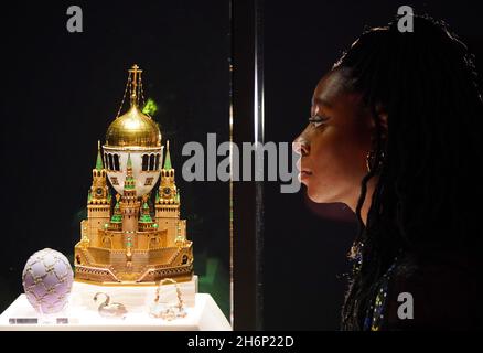 A museum employee looks at a display case containing the Moscow Kremlin Egg (centre) and the Swan Egg (left) during a photo call for the Victoria and Albert Museum's forthcoming exhibition 'Faberge in London: Romance to Revolution'. Picture date: Wednesday November 17, 2021. Stock Photo