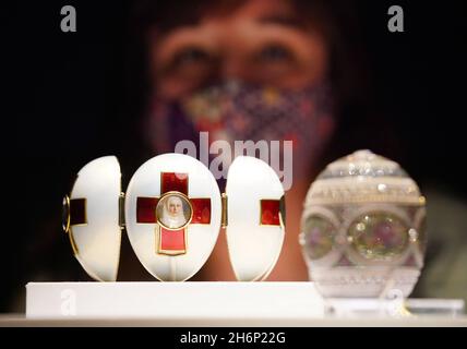 A museum employee looks at a display case containing the Red Cross with Tryptich Egg (left) and the Mosaic Egg (right) during a photo call for the Victoria and Albert Museum's forthcoming exhibition 'Faberge in London: Romance to Revolution'. Picture date: Wednesday November 17, 2021. Stock Photo