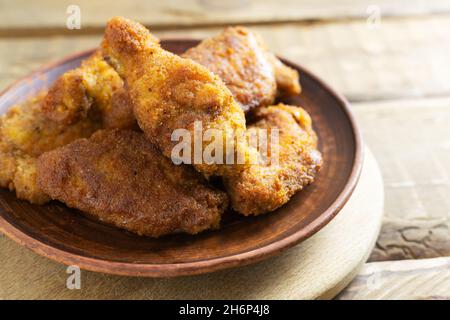 Crispy chicken wings and legs, breaded, cooked in oil in a ceramic plate on a wooden background. Junk food concept. Stock Photo