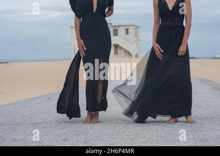 Two woman in black dresses seen standing on road Stock Photo