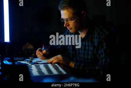 Male numismatist examines collection of coins. Stock Photo