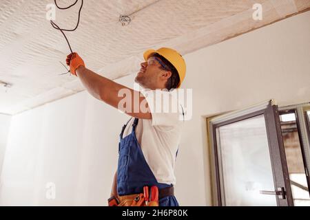 Joyful male electrician repairing electric cable on ceiling Stock Photo