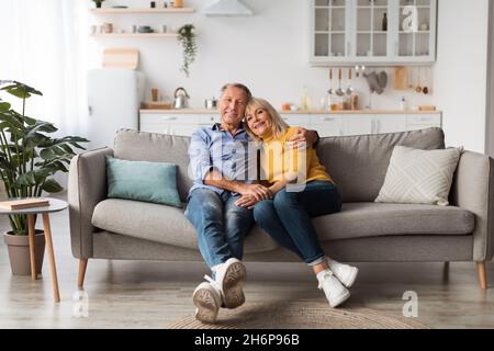 Happy Mature Couple Embracing Posing Sitting On Couch At Home Stock Photo