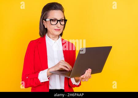 Photo of agent old brunette lady type laptop wear eyewear red cardigan isolated on yellow color background Stock Photo