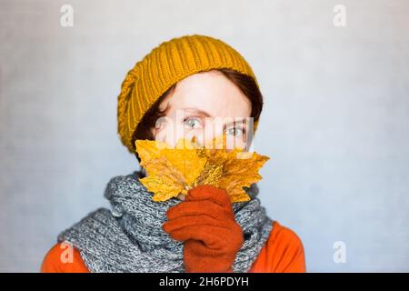 Beautiful happy woman wearing knitted clothes holds autumn yellow leaves near the face. Autumn season, knitting or fashion clothes concept. Stock Photo