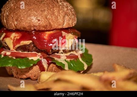 Delicious tasty grilled home made burger with beef,cheese,bacon and sauce on wooden table with copy space. Hands holding burgers with french fries and Stock Photo