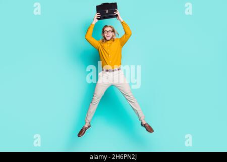 Full body photo of young guy happy positive smile have fun jump up hold suitcase bag isolated over turquoise color background Stock Photo