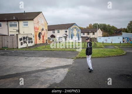 Young man  walking in front of political murals with paramilitary symbols on the Lower Shankill Estate, Belfast. Stock Photo