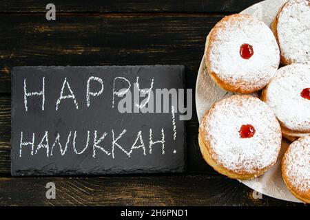 Happy Hanukkah. Traditional dessert Sufganiyot on dark wooden background. Donuts, candles and gifts. Celebrating Jewish religious holiday. Stock Photo