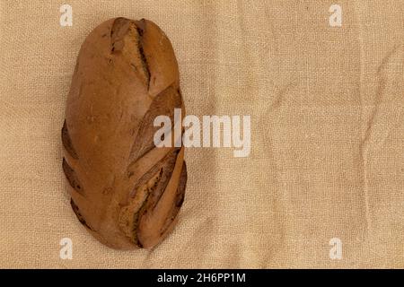 whole loaf of rye bread isolated on burlap, top view, space for text Stock Photo