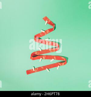 Minimal winter composition made of red Christmas ribbon and white pills on mint green background. Creative holiday depression concept. Stock Photo