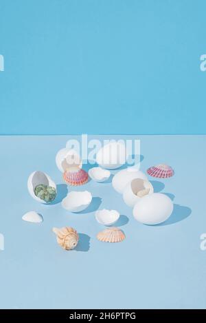 2021 Easter creative still life composition with colorful sea shells coming out of cracked white eggs. Modern, minimal background. Stock Photo
