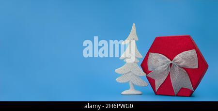Big red box with silver bow and shiny Christmas tree on blue background. New Year. Copy space Stock Photo