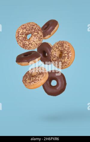 Donuts topped with white and dark chocolate and sprinkled with chocolate crumbs flying on blue background. Creative dessert and sweet concep Stock Photo