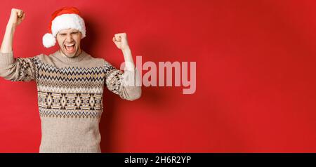 Satisfied handsome man, feeling lucky and happy, shouting for joy and making fist pumps, celebrating victory or win, receive awesome christmas gift Stock Photo