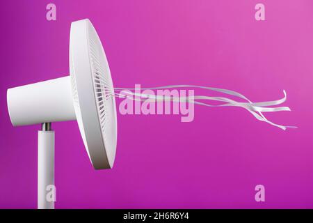 The electric fan is white with pink ribbons fluttering in the wind on a pink background. Free space, minimalistic style. Stock Photo