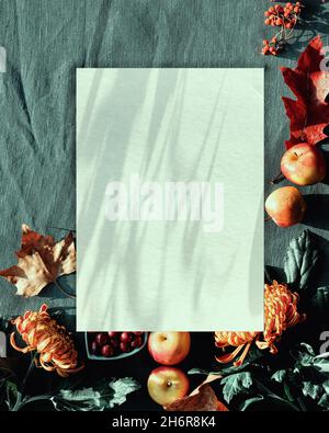 Paper mockup with shadows. Autumn decorations - cranberry, cookies. tea and dry oak leaves and wrapped gift. Flat lay, top view on dark green textile Stock Photo