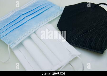 Comparison of various types of masks, the hygienic mask (blue), a three-layer mask (white) and an FFP2 mask (black) on a table Stock Photo
