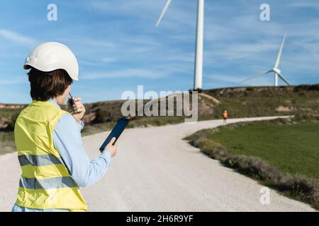 People working at green alternative energy farm with wind turbine power generators on background - Focus on woman back Stock Photo
