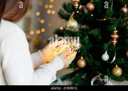Christmas miracle - woman in white sweater holds glowing led light garland in hands, bokeh background.