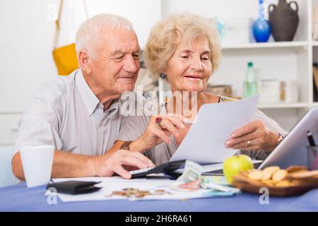 Happy senior spouses with bills and laptop Stock Photo