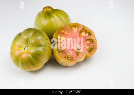 Close-up of three green Valencian tomatoes of the mascle variant, one of them cut in half, on white background Stock Photo