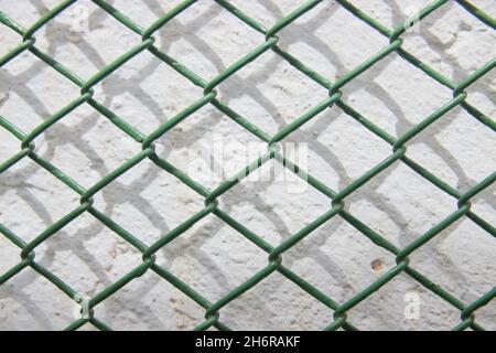 Closeup of a green grid that forms small rhombuses just in front of a rough white wall Stock Photo
