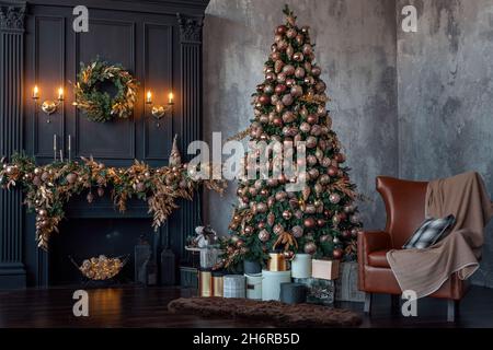 Big beautiful Christmas tree decorated with golden and beige shiny baubles and many different presents. Illuminated fir tree near the fireplace at home. New Year's eve and winters holiday concept. Stock Photo