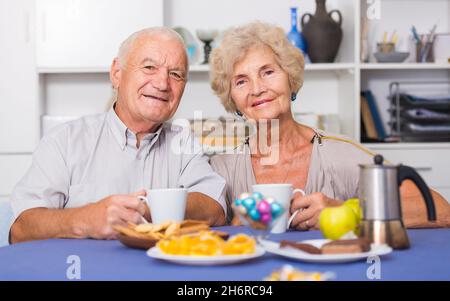 Smiling elderly spouses enjoying tea with sweets Stock Photo